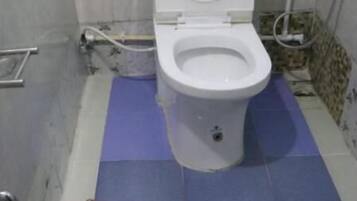 Une salle de bain avec des toilettes blanches, un tapis de sol bleu et un seau contenant un liquide rouge.