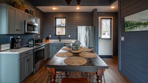 Une cuisine moderne avec des meubles gris, des appareils en acier inoxydable, une table à manger en bois avec des sets de table, et une grande carte du monde peinte au plafond.