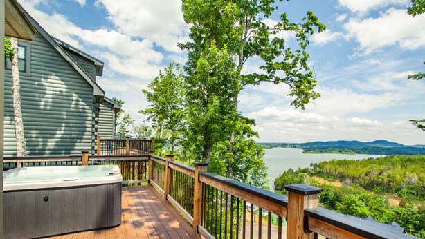 Une terrasse en bois avec un jacuzzi, offrant une vue sur un lac et une zone boisée.