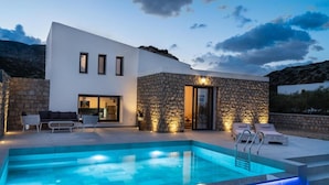 Una casa moderna con piscina, paredes de piedra y mobiliario de exterior.