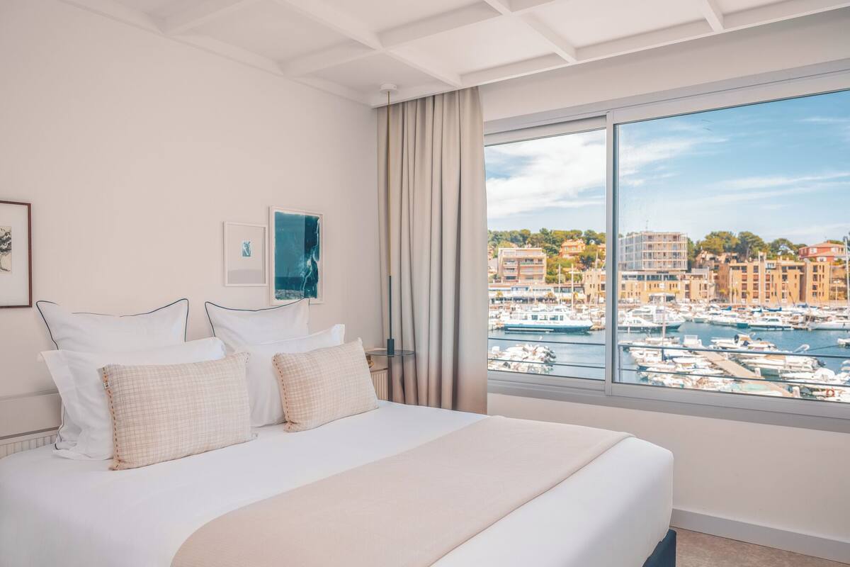 Un cuarto de hotel con una cama grande, vista al puerto deportivo y al paisaje urbano.
