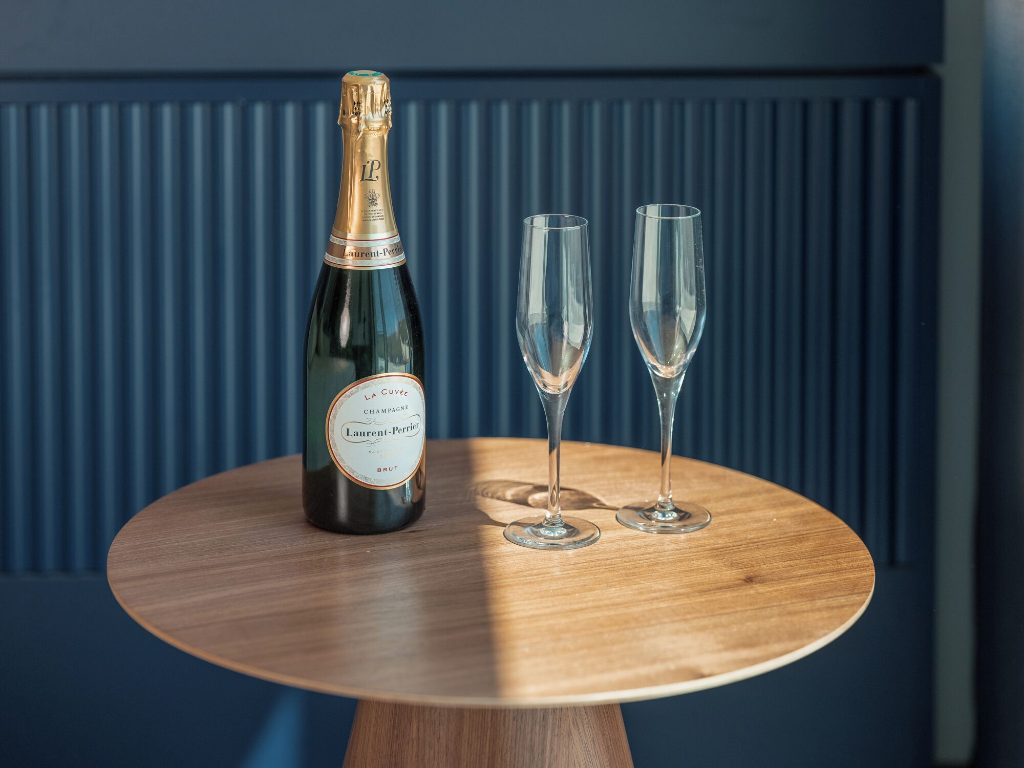 Una botella de champán y dos copas sobre una mesa de madera con un fondo azul.