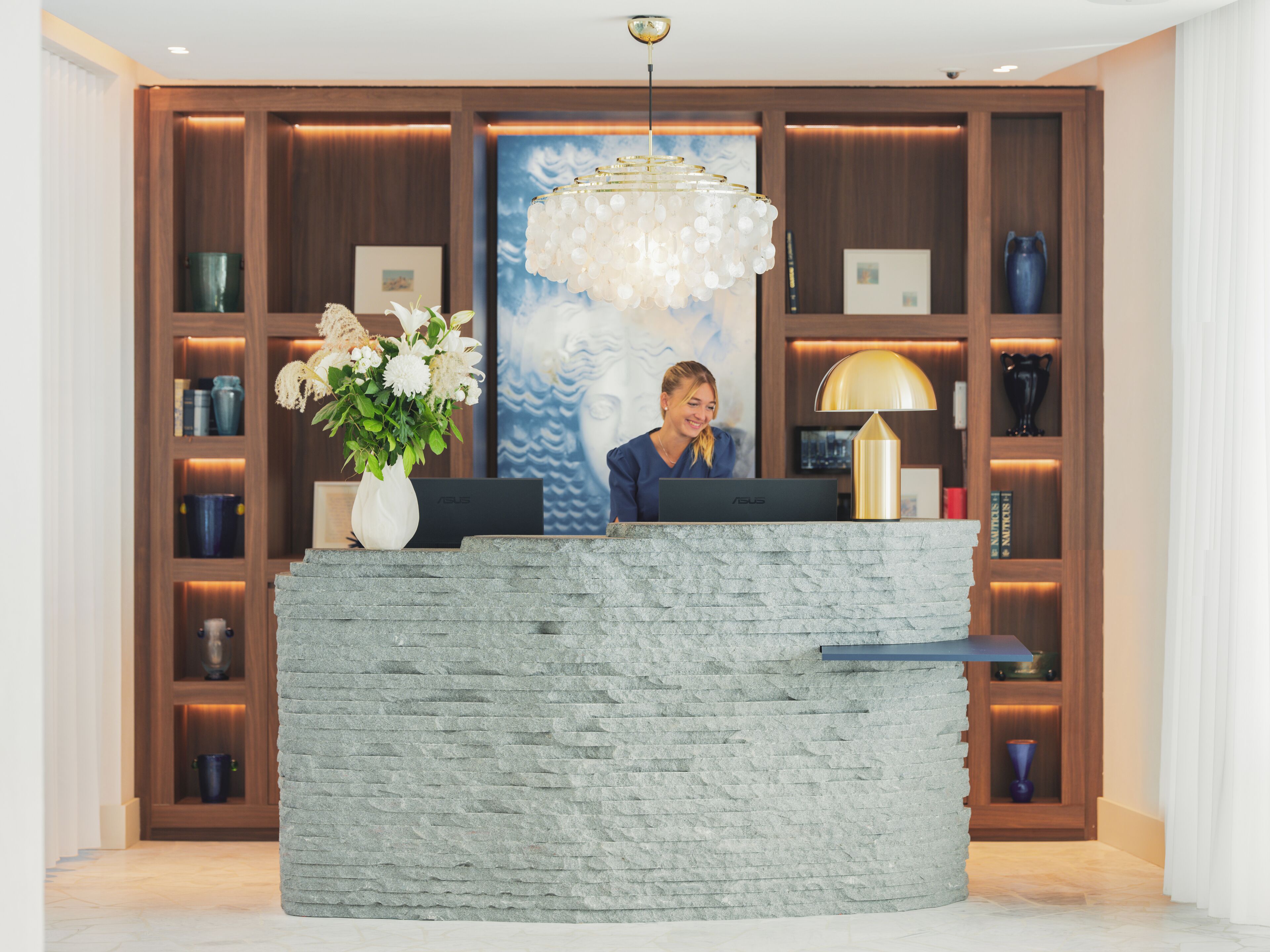 A reception desk with a laptop, a vase of flowers, and a large abstract painting in the background.