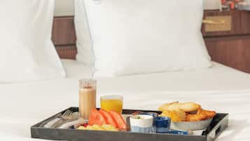 A neatly made bed with white pillows and a tray of breakfast items including croissants, fruit, and a beverage.