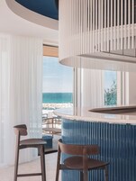 Un espace bar moderne avec un comptoir incurvé, deux tabourets de bar en bois et une grande fenêtre donnant sur une plage.
