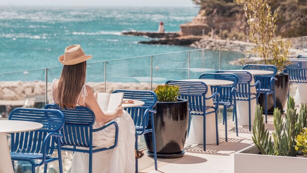 Una persona asseguda a taula amb vista al mar i un far a la distància.