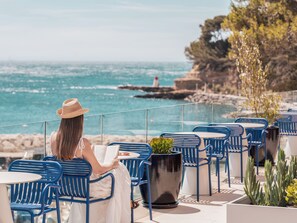 Una persona sentada a una mesa con vista al mar y un faro a lo lejos.