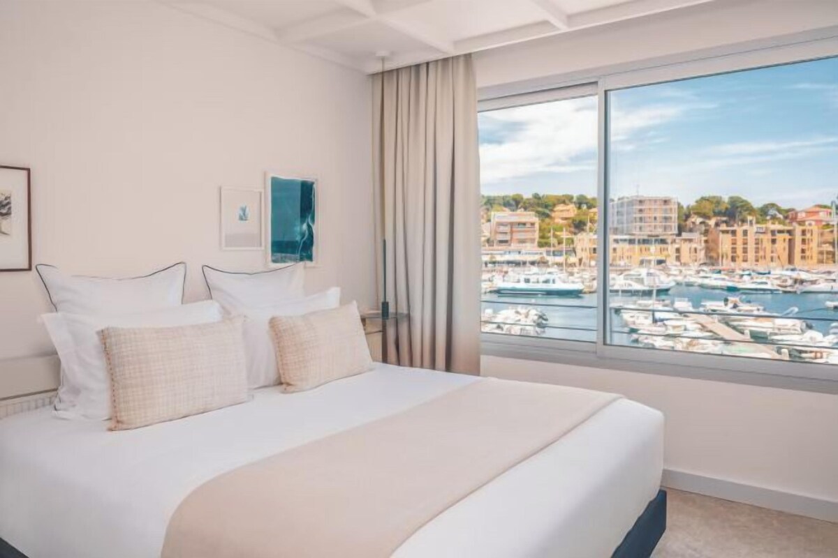 A hotel room with a large bed, a view of a marina, and a cityscape.