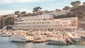 Una marina amb diverses embarcacions amarrades, un edifici amb la inscripció "BLEU" al fons, i un cel serè.