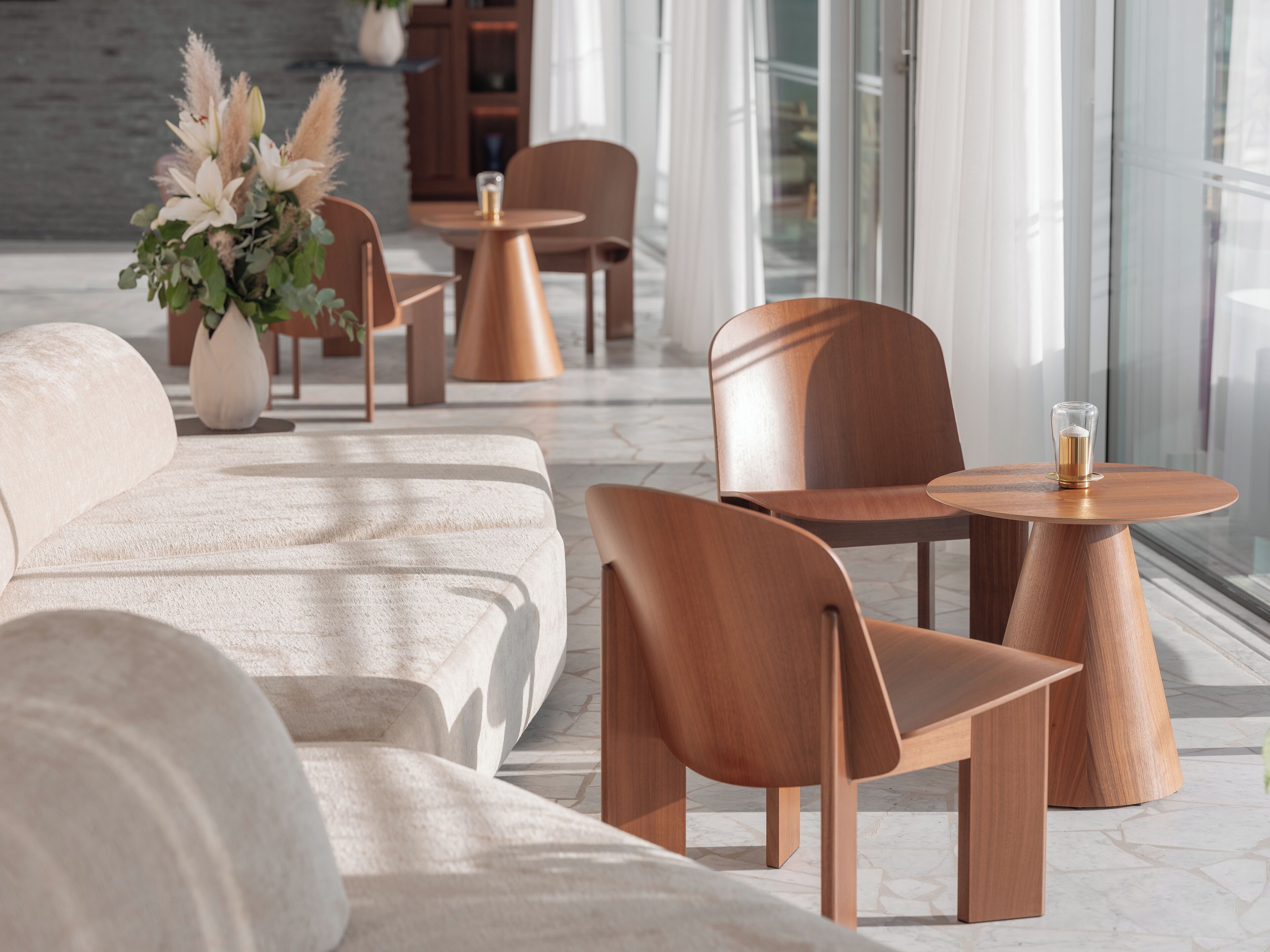 A modern lounge area with a sofa, wooden chairs, and a small table with a glass.