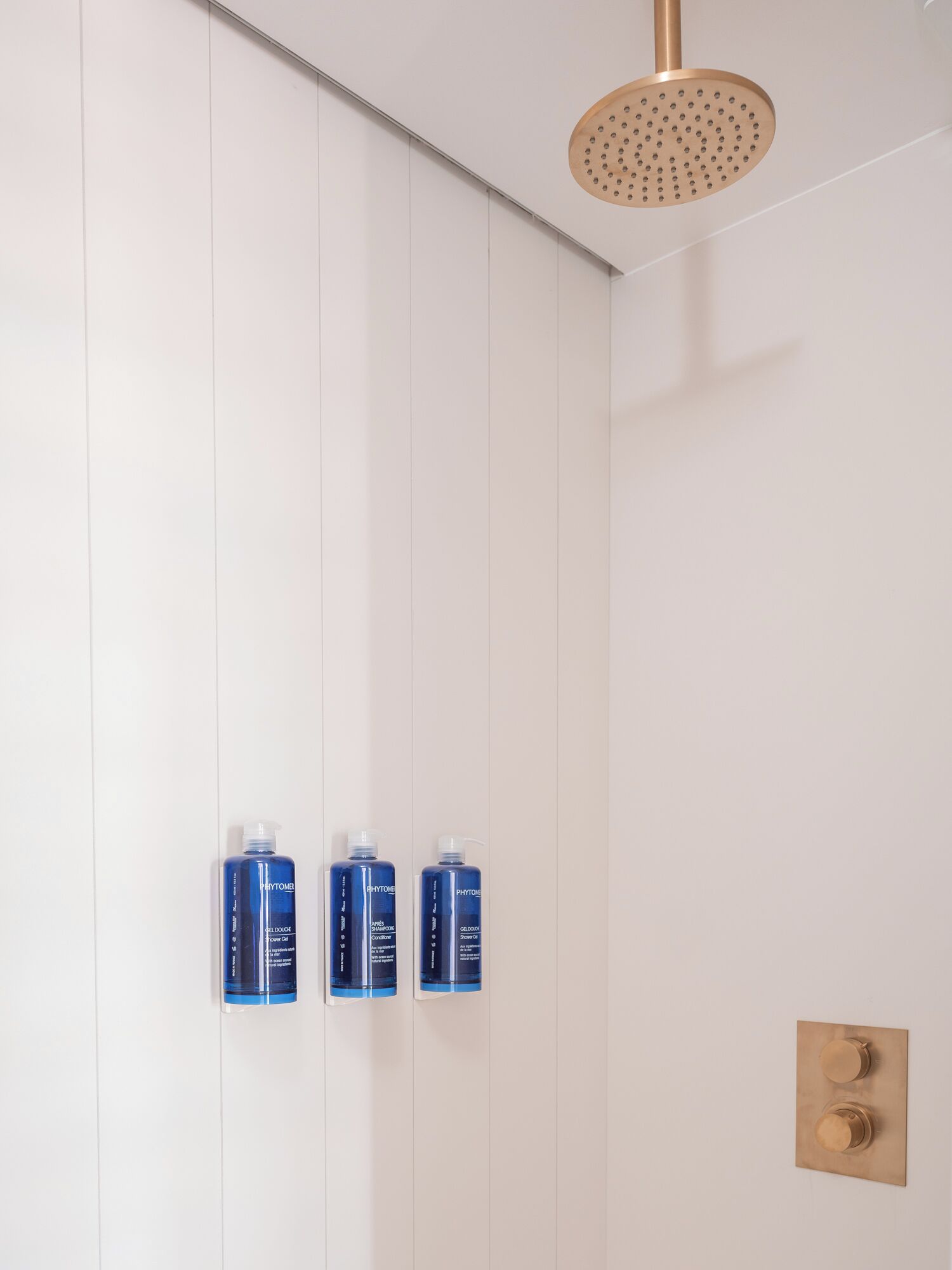 A shower with a gold showerhead and three blue bottles of Phytomen products on the wall.