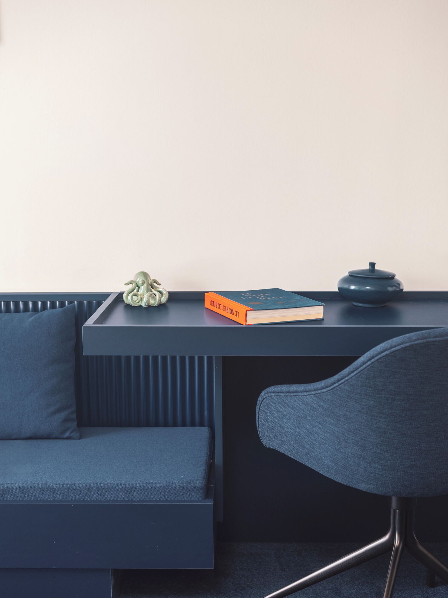 A modern room with a dark blue sofa, a matching chair, and a small table with a book and a decorative item.
