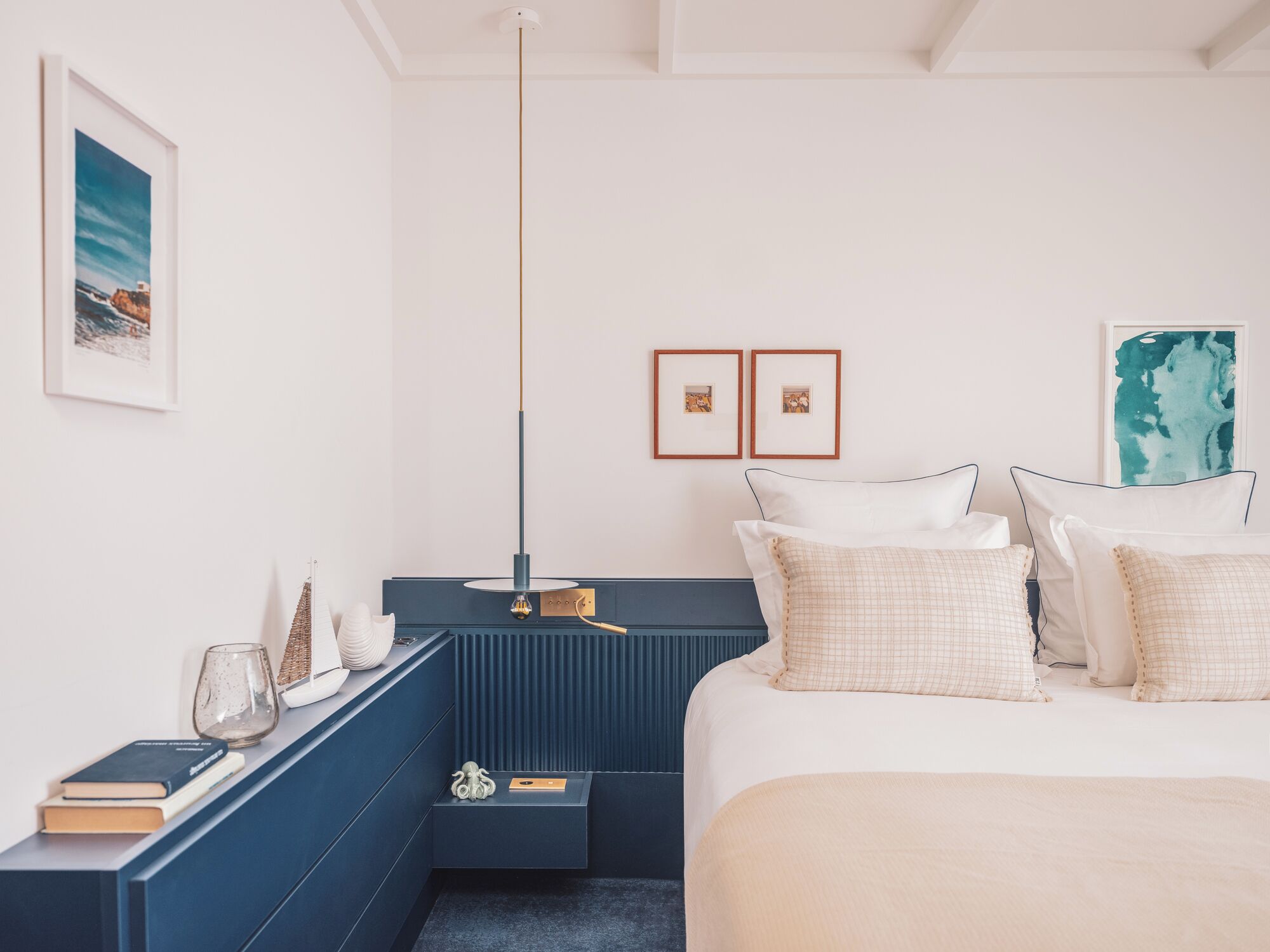 Ein Schlafzimmer mit einem Bett, Nachttischen, einer Nachttischlampe, einer Pendelleuchte und gerahmten Bildern an der Wand.
