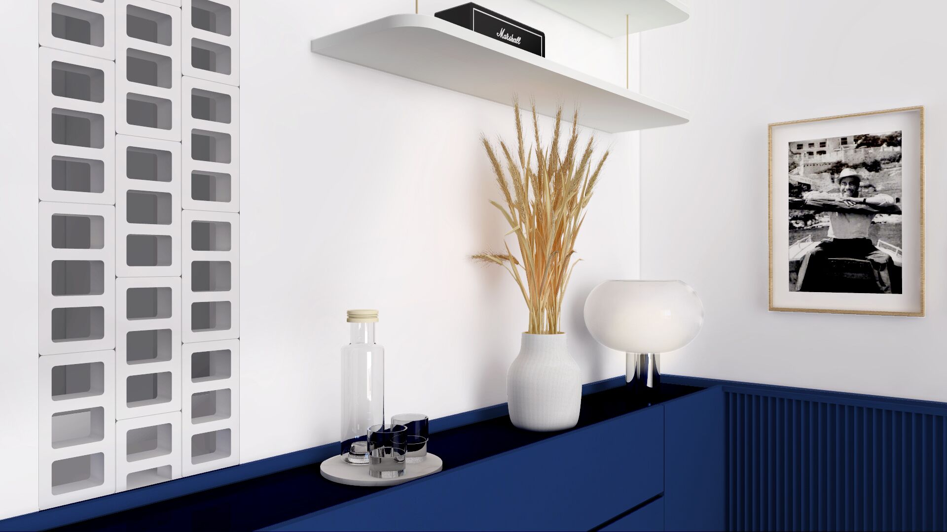 Et moderne køkken med hvidt bagpanel, en hvid vase med tørrede planter, en hvid bordlampe og et sort-hvidt billede i ramme på væggen.