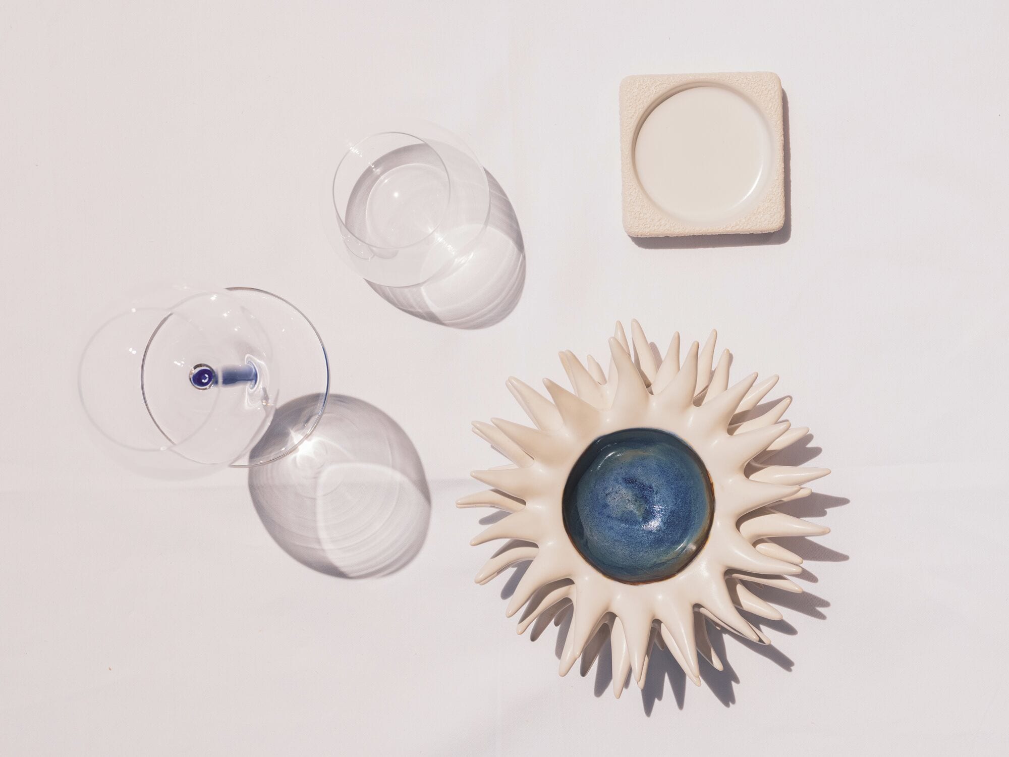 Three wine glasses, a ceramic plate, and a decorative sunburst object.