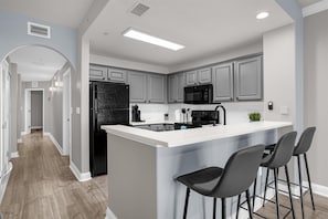 A modern kitchen with grey cabinets, a black refrigerator, a microwave, and a large island with bar stools.