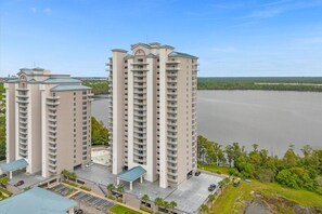 A high-rise building with multiple balconies, a parking area, and a view of a large body of water.