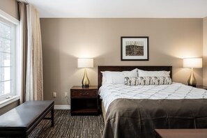 Une chambre d’hôtel avec un lit, des lampes de chevet, un banc, un tableau encadré au mur et une fenêtre avec des rideaux.