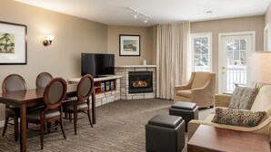 A living room with a fireplace, a television, a dining area with chairs, and a sofa with a patterned pillow. - Horseshoe Valley Suites - The Glade (Oro-Medonte)