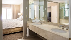A hotel bathroom with a large mirror, two sinks, a bed, and a window with curtains. - Horseshoe Valley Suites - The Glade (Oro-Medonte)
