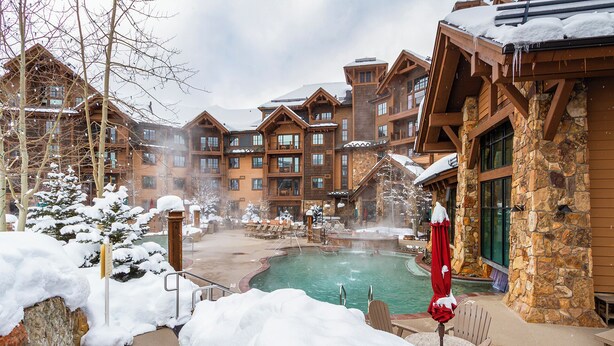 Un resort con piscina, edificios de madera y alrededores nevados.