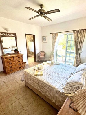 Een slaapkamer met een bed, een dressoir, een plafondventilator, een raam met gordijnen en een deur naar een andere kamer.