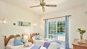 A bedroom with two beds, a ceiling fan, a window with curtains, and a view of a swimming pool. - Vista da Montanha - Three Bedroom Villa, Sleeps 6 (Carvoeiro)