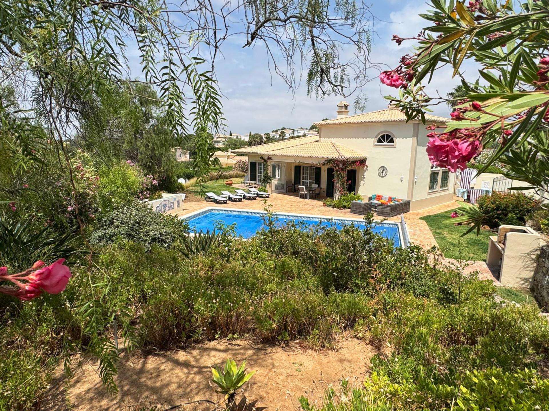 A house with a swimming pool, surrounded by lush greenery and a garden.