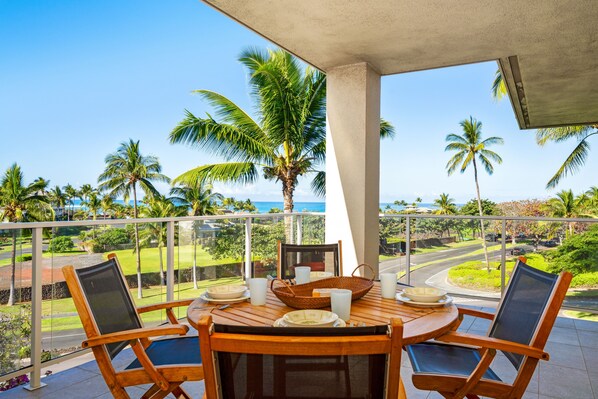 A wooden table with chairs on a balcony overlooking a scenic view of palm trees and a road.