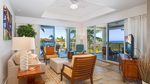 A spacious living room with a large window, a ceiling fan, a sofa, a wooden chair, a coffee table, and a television.
