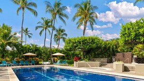 A swimming pool with clear blue water, surrounded by palm trees and lounge chairs.