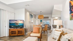 A modern living room with a flat-screen TV, comfortable seating, and a dining area.