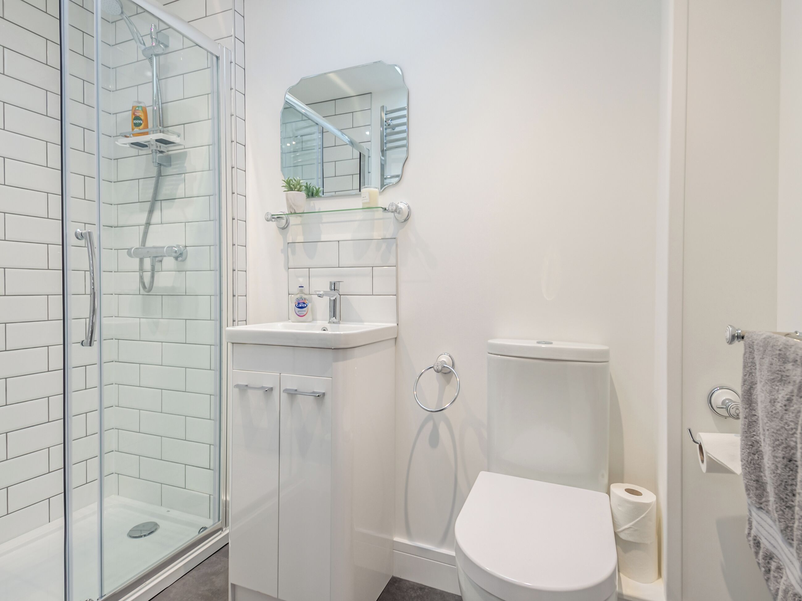A modern bathroom with a glass shower enclosure, a white toilet, and a sink with a mirror above it.