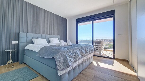 Un dormitorio moderno con una cama grande, vista de la ciudad desde un balcón y un ventanal amplio.