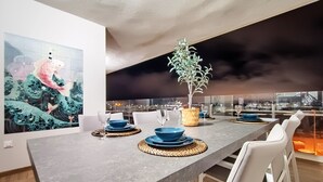 Un comedor moderno con una mesa larga, vajilla azul y vista nocturna a la ciudad.