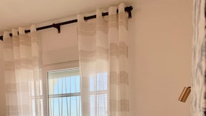 Ein Schlafzimmer mit einem großen Bett, einem Fenster mit Blick auf eine Stadtlandschaft und transparenten Vorhängen.