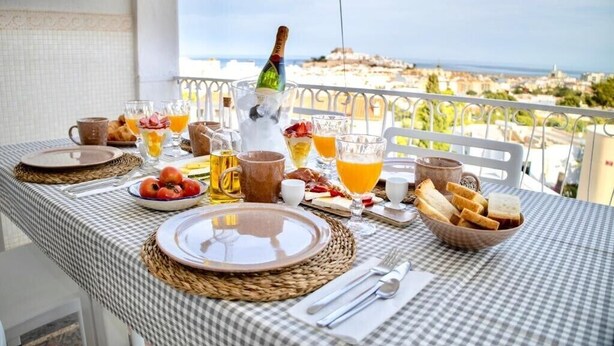 A table set for breakfast with a view of the sea, including plates, glasses, and a bottle of champagne. - Apartamento 2 (Peníscola)