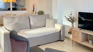 A modern living room with a grey sofa, two armchairs, a TV, and a decorative lamp. - Apartamento 2 (Peníscola)