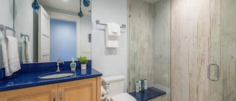 Un baño moderno con encimera azul, armarios de madera, inodoro blanco y cabina de ducha con mampara de cristal.