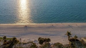 Een strand met een heldere lucht en de zon die op het water glinstert.