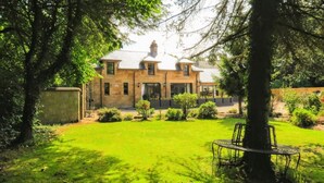 A two-story stone house with a well-maintained lawn and a tree in the foreground. - Renovated characterful coach house close to Loch Lomond and Helensburgh (Cardross)