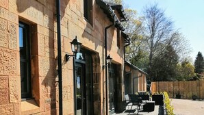 A stone building with a wooden deck, outdoor seating, and a wooden fence. - Renovated characterful coach house close to Loch Lomond and Helensburgh (Cardross)