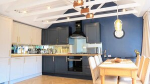 A modern kitchen with dark cabinets, a wooden countertop, and a dining area with a table and chairs. - Renovated characterful coach house close to Loch Lomond and Helensburgh (Cardross)