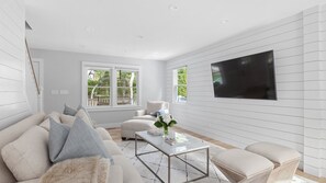 Uma sala de estar moderna com um sofá, poltronas, uma mesa de centro e uma TV fixada na parede.