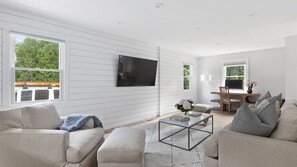 Uma sala de estar moderna com uma TV de tela plana na parede, uma mesa de centro com um vaso, e um espaço de estar com dois sofás.