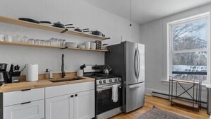 A modern kitchen with white cabinets, a stainless steel refrigerator, a gas stove, and wooden countertops. - Lawless Rico: Enterprise Suite (Rico)