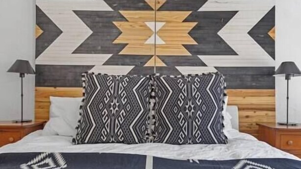 A bed with patterned pillows, a wooden headboard, and a geometric wall design. - Lawless Rico: Enterprise Suite (Rico)