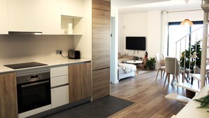 Eine moderne Küche mit integrierten Geräten, ein Essbereich mit weißem Tisch und Stühlen sowie eine Treppe, die zu einer oberen Ebene führt.