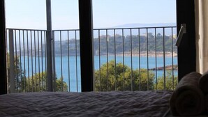 Ein Schlafzimmer mit großem Fenster mit Blick auf ein Gewässer und sanfte Hügel in der Ferne.