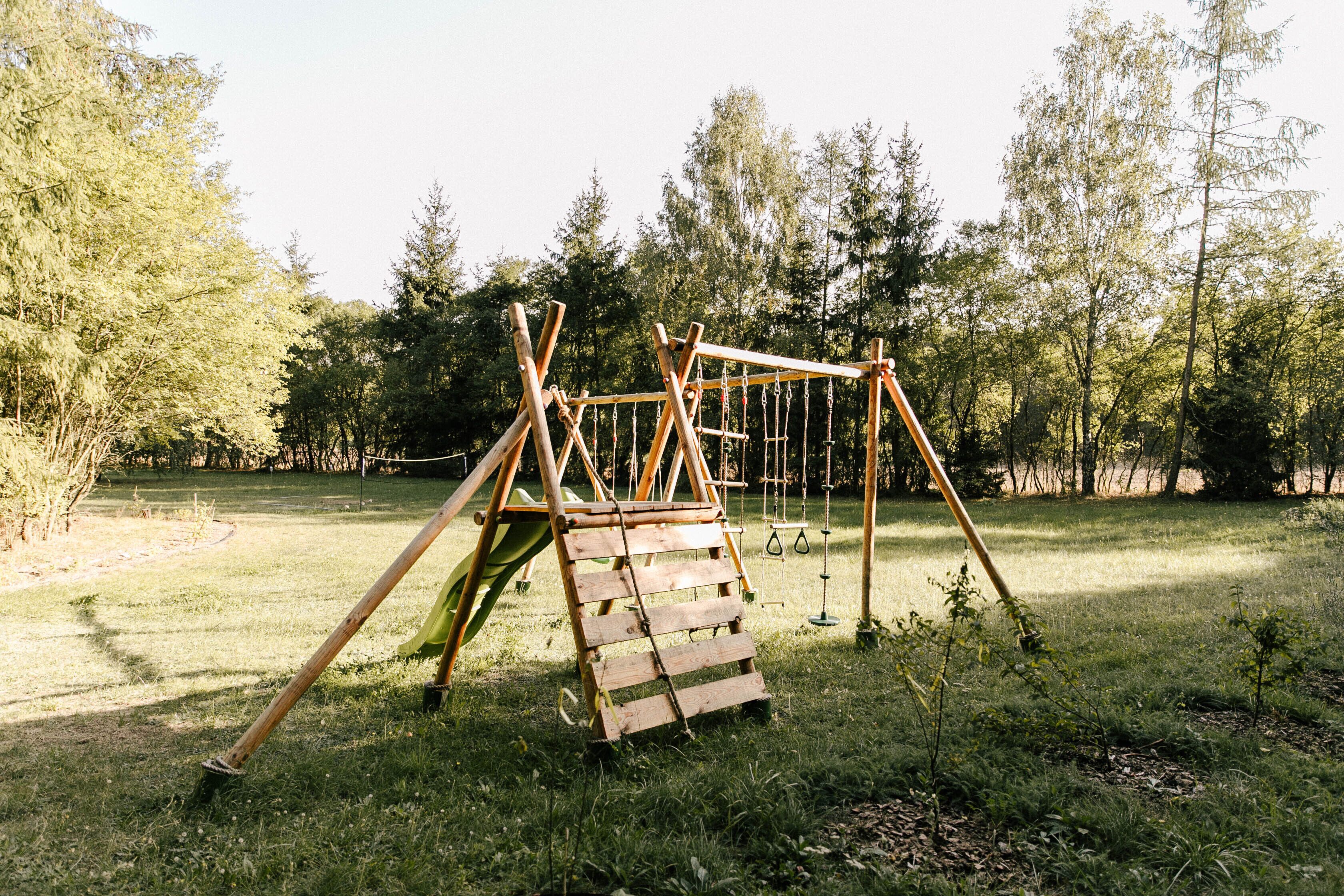 A wooden swing set in a grassy area with trees in the background.